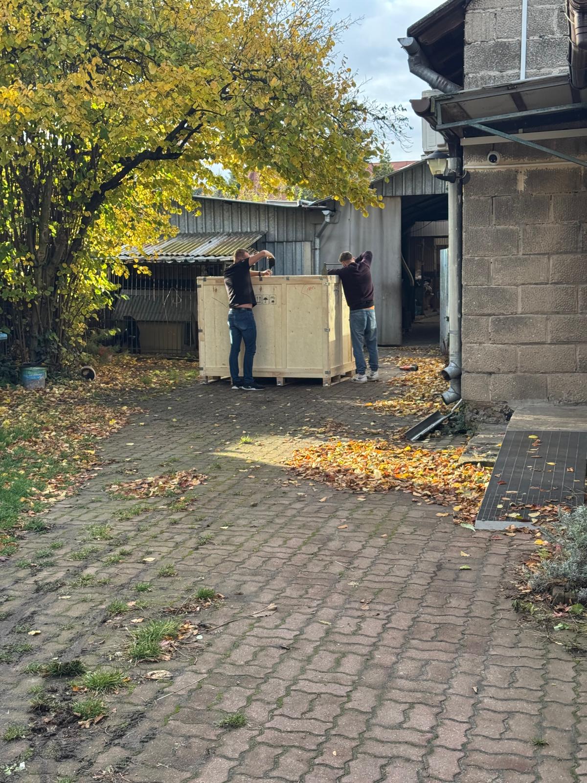 Pracownicy Najtrans wnoszący drewnianą skrzynię przez podwórze
