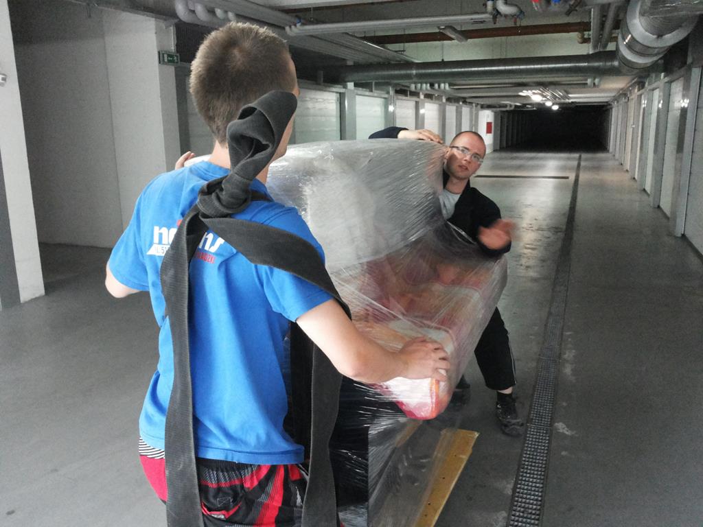 Pracownicy Najtrans niosą zafoliowany mebel w garażu podziemnym