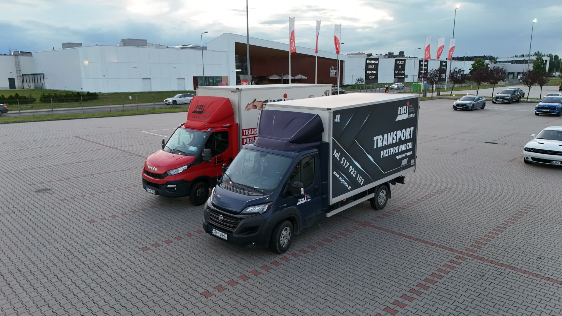 Dwa auta Najtrans - nowy granatowy i czerwony - na parkingu Designer Outlet Kraków