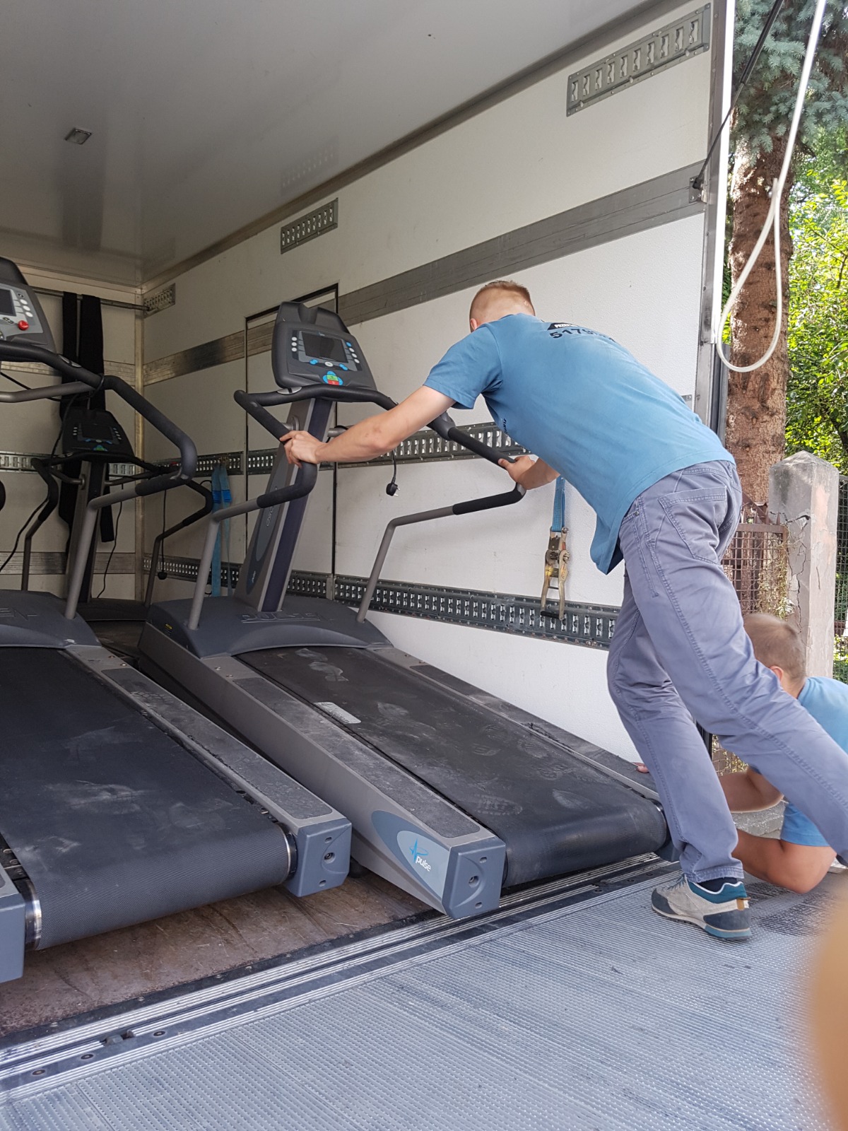 Pracownik Najtrans załadunek sprzętu fitness - bieżnie w aucie transportowym