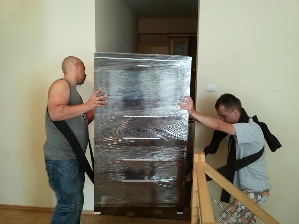 Pracownicy Najtrans przenoszą zafoliowaną komodę
