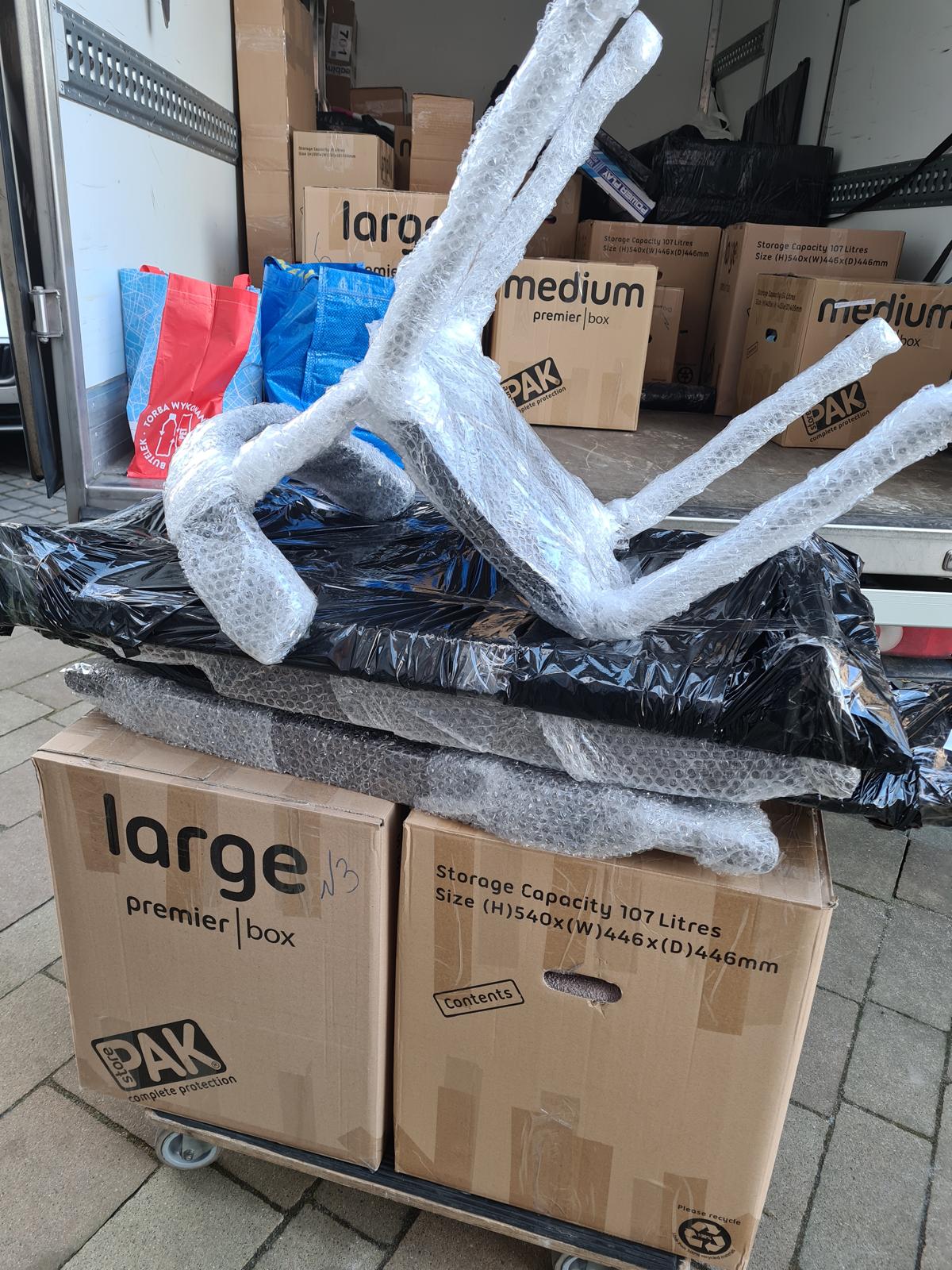 Zabezpieczone meble i kartony na wózku transportowym przy aucie Najtrans